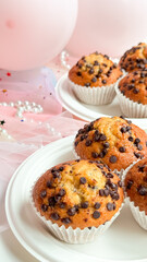 Chocolate chip muffins on white plates with pink background and balloons. Birthday concept