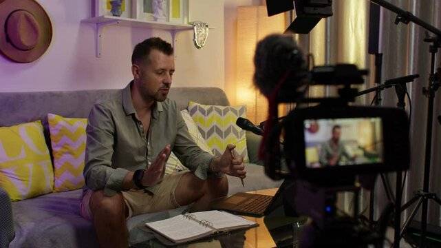 A person records a podcast at home, sitting on a couch in a cozy setup with lights