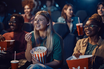 Happy woman eating popcorn while enjoying in film screening at movie theatre.