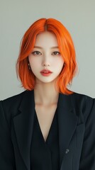 A professional portrait of a woman with striking orange hair, wearing a black blazer against a neutral background.