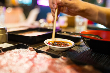 Hand man uses wood chopsticks mix and stir the dipping sauce for eating Thai style local hot pot  in outdoors restaurant