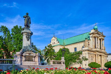 Obraz premium Monument to Adam Mickiewicz in the Adam Mickiewicz Square with colorful red and yellow flowers and blue sky on a summers day, Warsaw, Poland, Europe