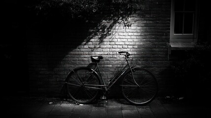 Obraz premium Monochrome image of a vintage bicycle parked against a brick wall at night, illuminated by a spotlight.