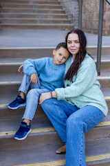 This heartwarming portrait shows a joyful young boy enjoying a moment with his caring mother. They are casually dressed, relaxed, and sitting on outdoor stairs, enjoying nature together