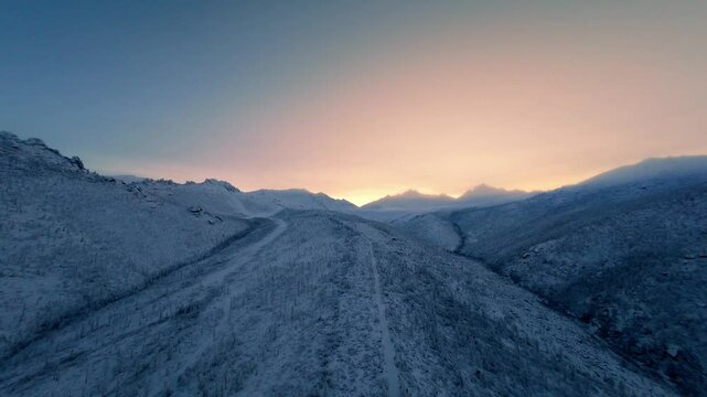 A breathtaking winter morning reveals a stunning sunrise illuminating the snow-covered landscape. The serene view showcases mountains and valleys, creating a peaceful atmosphere in nature.