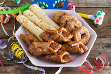 Typical carnival desserts with carnival decorations on a wooden background.