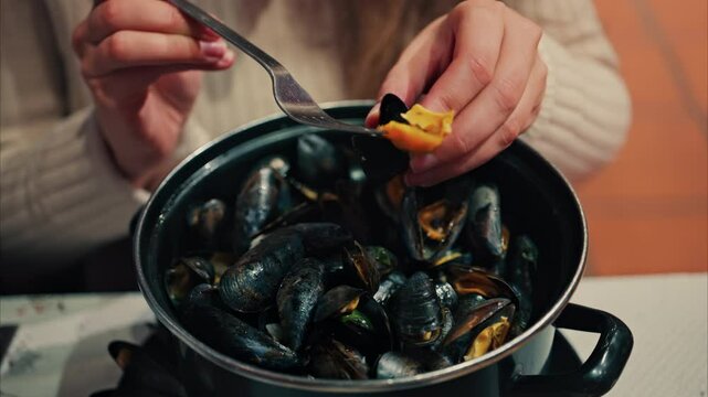 Close up of a woman eating mussels from a pan with a fork