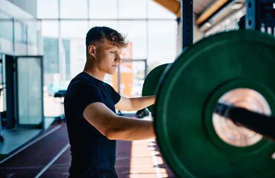 Fit young man in sportswear preparing to do a strength training workout session using heavy weights alone at the gym