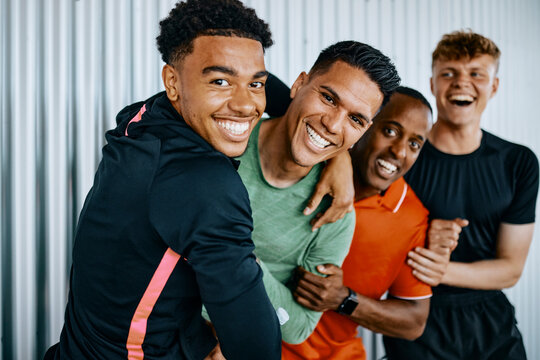 Diverse group of fit young men in sportswear laughing and messing around together while standing arm in arm together in a gym after a workout session together