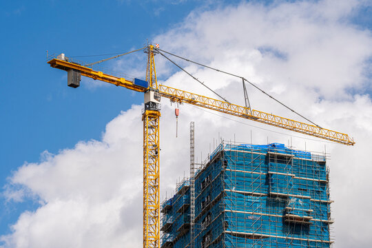 The image depicts a construction site featuring a towering crane and scaffolding around a building, symbolizing growth, infrastructure development, and urban transformation.