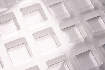 An industrial transparent square thermoforming mold made of plastic as a packaging solution for industrial products. Foil cubes on a white background and shining lights.