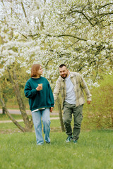 Fototapeta premium A couple strolls hand in hand in a park filled with blooming trees.