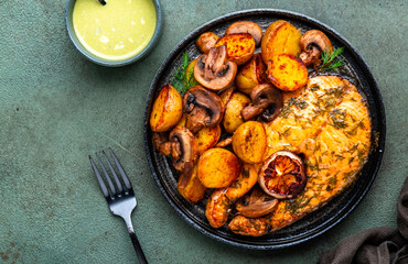 Baked salmon with lemon and dill, fried potatoes with mushrooms and cream sauce. Green rustic background, top view