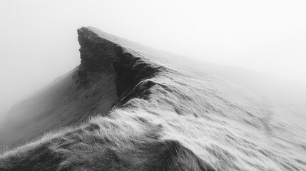 Dramatic black and white image of a snow-covered mountain ridge shrouded in fog.