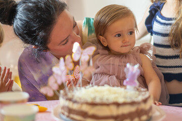 Mother lighting birthday candle for young daughter, capturing joyful first-year milestone with warm family moment