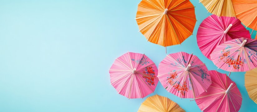 A set of multi colored cocktail drink umbrellas or paper parasols in vibrant pink and orange featuring floral designs against a light blue backdrop. with copy space image