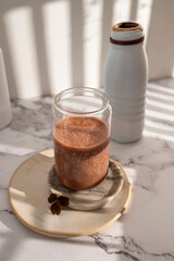 Creamy chocolate protein drink served in a clear glass beside its plastic bottle.