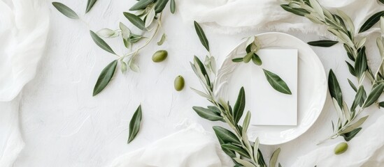 Wedding table setting featuring place cards and porcelain plates adorned with olive branches viewed from above Stylish modern template with a horizontal blank paper card flat lay Mediterranean mock