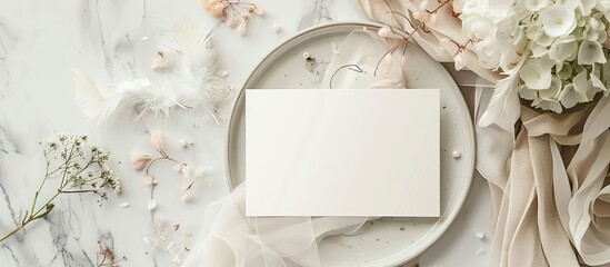 Wedding table setting featuring a blank card alongside flowers silk ribbons and feathers from a top view A romantic template showcases a vertical paper card on a plate placed on a marble table flat