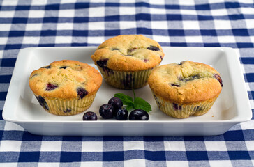 three blueberry muffins on rectangular plate on blue and white table cloth