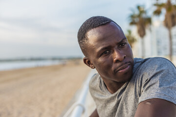 Fototapeta premium Portrait of young black man with sunset sky and palm trees on the promenade in the background
