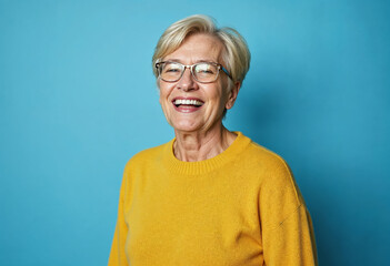 Portrait of a gray-haired mature woman in a yellow sweater on a blue background