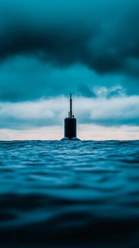 A close up of a submarines periscope breaking through the surface of a calm sea with ripples spreading outward under a cloudy sky 