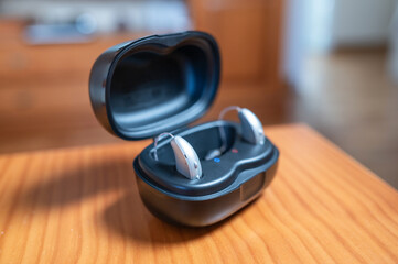 Hearing aid devices charging in modern case on wooden table