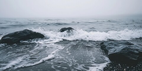 Naklejka premium A misty seascape featuring waves crashing against dark rocks.