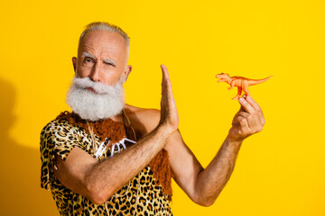 Portrait of primeval caveman arm reject deny tiny dino toy wear leopard skin outfit isolated on yellow color background