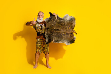Full length photo of handsome neanderthal guy wear leoprad skin rising animal prey fur showing thumb up emtpy space isolated yellow color background