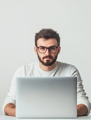 stylish young man with beard wearing glasses seated at modern laptop in minimalistic light gray workspace with ample empty copyspace for text