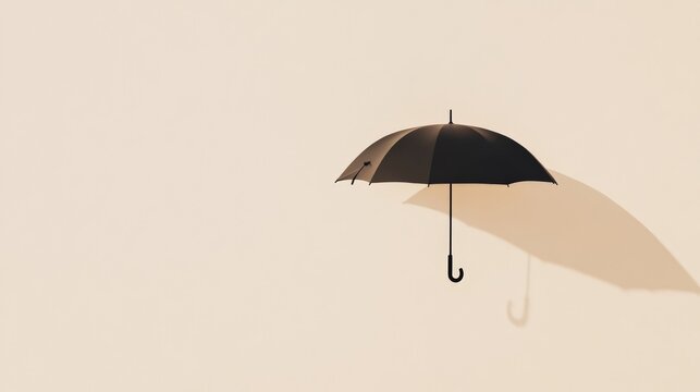 Black umbrella floating in the air with its shadow projected on a beige background, creating a surreal and minimalist composition with copy space