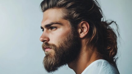 Obraz premium Profile portrait of a young adult man with long hair and a full beard against a neutral background, suitable for work-from-home themes with ample copyspace.