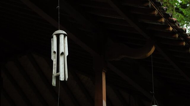 Bamboo wind Chimes hangs on traditional javanese house ceilings or wall against blue sky and agricultural fields backgrounds. Close-up of wooden wind chime in a garden.