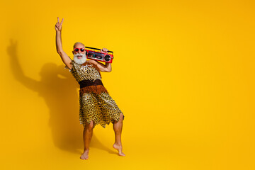 Full length photo of funny strong cave human wear leoprad skin enjoy boom box showing v-sign emtpy space isolated yellow color background