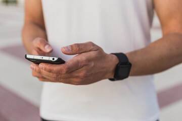 Muscular man resting on the beach promenade at sunset using his mobile phone after workout