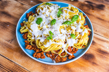 Spaghetti Bolognese pasta nests with Bechamel sauce and minced beef fried with tomatoes, onions and carrots on a blue plate on a wooden table. Top view. Copyspace or space for text.