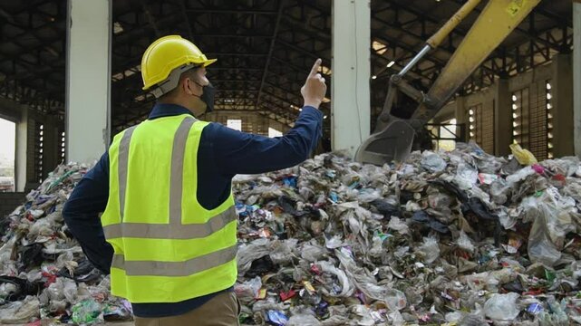 A environmental engineers are checking the quality of waste in a waste sorting plant with a backhoe in the background.