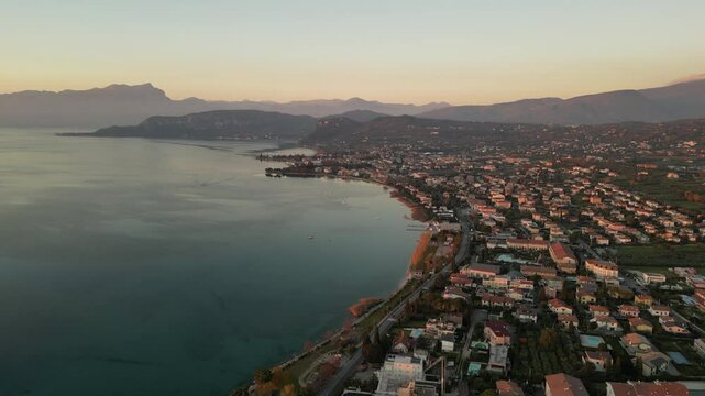 horizontal smooth drone video of Garda Lake at golden hour and villages nearby with traditional red roofs Bardolino, Garda with rocks 