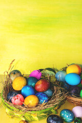 Colorful easter eggs in a basket on a yellow wooden table. Vertical photo