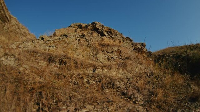 Rocky hillside with dry grass under a clear blue sky. Natural outdoor landscape.