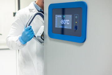 Scientist opening cryogenic freezer in laboratory wearing lab coat and gloves