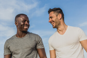 One Caucasian and one Black man laughing together on the beach after exercising