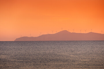Wind turbines sunset. Seaside landscape with a wind turbine farm on a mountain. Green energy electricity source. Concept image for eco energy.