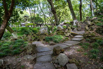 A traditional Chinese landscape in a public park, featuring shaded pathways, ornamental rock formations, and lush green trees. An inviting environment at Zhongshan Park. Ningbo, China