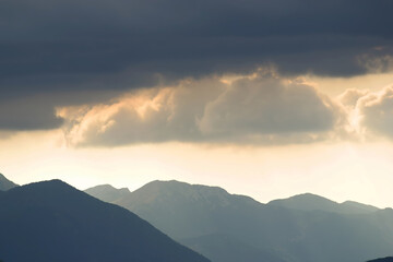 The sun shines through the clouds with outlined silhouettes of the Velebit mountains, Croatia