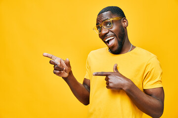 Happy young man in a yellow t shirt pointing with enthusiasm against a bright yellow background, showcasing confidence and joy, perfect for lifestyle and fashion concepts