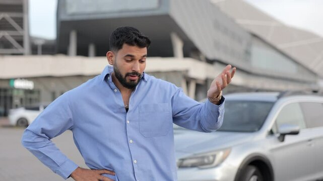 Young upset driver man in front of automobile broken car collision accident in city road. Tired, disappointed guy with hand on head, shaking head in confusion. Concept of car crash, emotions, broken.