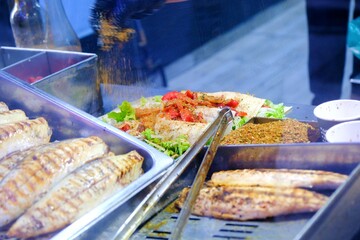 Turkish street food and grilled fish - fish bread. Close up. Chef cooks fish on the barbecue with tongs. Tomatoes are placed in the wrap. Food industry. Fast food. Karakoy - Istanbul. Turkey.